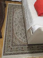 Full view of the Semerkant Oriental wool area rug laid out beside a sofa and wooden floor, showing the entire rug and part of adjacent furniture.