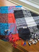 Two pashmina silk scarves side by side on a wooden surface showing their patterns and fringed ends.