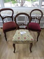 Front view of the set of three Victorian style chairs showing two red velvet seats and one floral needlepoint seat with wooden carved backs and legs.
