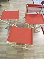 Top view of four foldable stools with natural wood frames and red canvas seats arranged on wood floor.