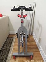 Front view of the indoor exercise bike showing the padded handlebars and saddle seat with silver frame base and red wheels.