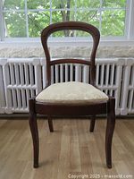 Front view of Victorian style wooden chair showing curved backrest and cream upholstered seat with floral pattern.