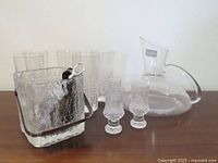 Photo of vintage barware items including ice bucket, wine goblets, decanter, small crystal glasses, and opener on wooden surface