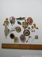 Full view of 21 pieces of vintage costume jewelry: various pins, brooches, earrings, tie pins featuring gold-tone, silver-tone, enamel, and rhinestones.