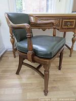 Side angle view of vintage wooden armchair with green leather upholstery showing the armrest, seat, and leg stretcher details.