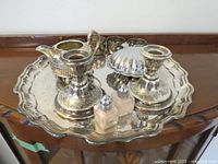 Full view of the entire silver-plated serving set on scalloped tray including lidded butter dish, candle holders, cream jug, sugar bowl, salt and pepper shakers.