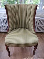 Front view of a vintage accent chair featuring green striped fabric upholstery, wood frame, and brass nailhead trim, showing overall condition and style.