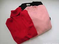 Lot of 3 folded cashmere sweaters in pink, red, and black colors showing overall condition.