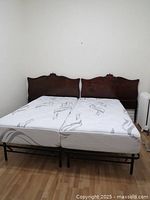 Two wooden twin/king headboards shown attached to twin mattress frames, placed side by side on a wood floor against a white wall.