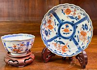 Image of Chinese Imari tea bowl and plate on wooden display stands showing hand-painted cobalt blue and orange floral patterns.