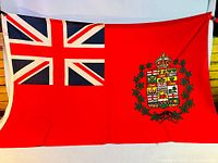 Full view of Canadian Red Ensign flag showing Union Jack canton and coat of arms shield on red background.