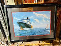 Framed offset lithograph print of the Queen Mary 2 ship displayed on the ocean, with glass and red inner matting visible in the frame.