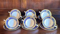 Six bouillon cups paired with their six matching saucers arranged on a wooden surface showing full set.