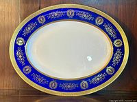 Top-down view of the oval serving platter showing cobalt blue border with gold encrusted floral and leaf patterns and white center.
