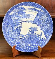 Front view of large round charger plate with blue and white Asian style designs, displayed on a wooden stand.