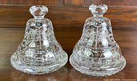 Pair of clear Waterford crystal commemorative bells for Cunard Cruise Line 150th anniversary on wood background.
