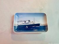 Top view of the rectangular porcelain tray featuring a ship painted in blue, white, and black on the ocean with small sailboats and detailed sky.