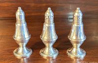 Three vintage sterling silver weighted salt and pepper shakers placed in a row on a wooden surface.
