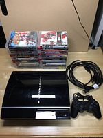 PlayStation 3 console, controller, power cable, HDMI cable and stacked video games arranged neatly on floor