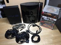 Photo of Playstation 3 console, Playstation 2 console, stack of video games with discs, and several cables