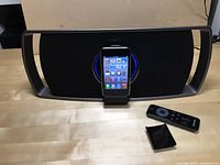 Phillips speaker dock with Apple iPod Touch placed vertically in dock, remote control and dock adapter piece on table.