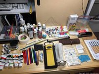 Full layout of assorted art supplies on table showing paints, coloured pencils, brushes, and painting tools.