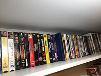Photo showing a lineup of DVD and VHS movie cases on a shelf including titles such as Mona Lisa Smile, Ghost, Terminator 2, Jurassic Park, and Titanic
