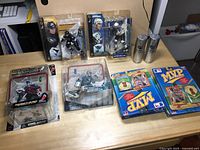 Photo showing five McFarlane NHLPA Series 1 hockey action figures in original packaging, two silver cans likely containing baseball pins, and two sealed MLB MVP Series baseball card packs.
