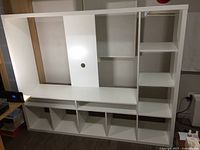 Disassembled white LAPPLAND TV stand and shelf unit laid against wall showing shelves, base cubbies, and vertical panel with cable hole.