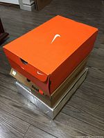 Stack of three shoe boxes on floor, orange Nike box on top.