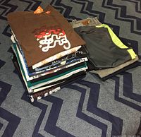 Stack of folded t-shirts and pants/jeans showing colors and some logos