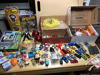 Wide view of the assorted toy figures, cars, collectibles, and packaged items spread on a table.