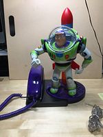 Full view of Buzz Lightyear figure integrated with purple corded telephone handset on base with rocket