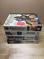Stacked view of four PC game boxes with titles visible along the side including Shogun Total War Gold, Fleet Defender Gold, Silent Service II, and Across Suez.