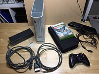 Full lot overview with Xbox 360 console, power brick, power cable, Kinect sensor, one controller, two video games in cases, and cables arranged on table.