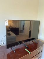 Front-side angle of the 43" TV on a wood dresser with power cable visible and remote placed in front