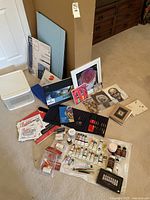 Photo showing assortment of acrylic and oil paints, brushes, notebooks, pads, framed photo, pastels, and storage boxes.