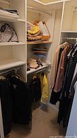Closet shelving with folded blankets, bags, multiple hats, and hanging dark men's suits and a yellow jacket