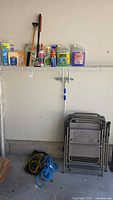 Photo of automotive cleaning liquids, sprays, brushes on a wire shelf with cleaning pole and folding chairs below.