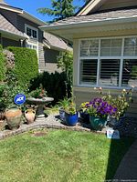 Full view of the birdbath, flower pots, terracotta jars, plants and gnome tile arranged on a stone-bordered garden bed