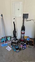 Garage floor overview showing two upright vacuums side by side with handheld vacuum, cleaning bottles and accessories