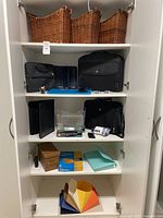 Full view inside white storage cabinet showing three wicker baskets on top shelf and three shelves of office, document, and bag items below.