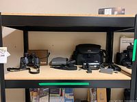 Overview of all items on shelf: camcorder with accessories, binoculars with case, Polaroid Spectra