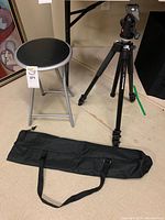 Full shot of tripod, foldable chair, and carrying bag placed on floor.