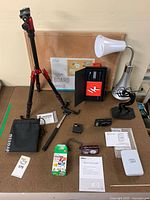 Overview of all lot items on desk: cameras, tripod, selfie stick, lamp, cork board, printer, film pack, paperweight