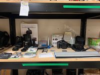 Shelf with Canon camera, lens accessories, cleaning kit, blank mini DVDs, and other camera related items.