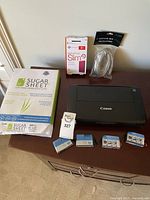 Canon Pixma TR150 printer, HP ink cartridges, Seagate 2TB drive box, USB cable and copy paper on table