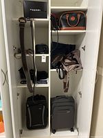 Cabinet with two carry on suitcases, handbags and backpacks on shelves and hanging straps