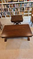 Dark brown wood coffee table and matching end table in a room with bookshelves and chairs, coffee table closed.