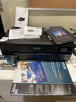 Printer front view with stacked photo paper and manuals on top